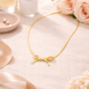 Gold bow pendant necklace styled on soft fabric background with floral accents