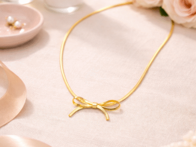 Gold bow pendant necklace styled on soft fabric background with floral accents