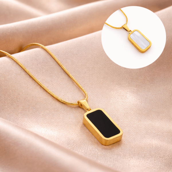 Gold black and white reversible bar pendant necklace styled on soft fabric background